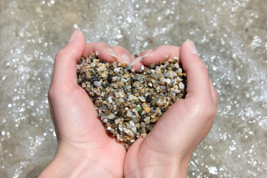 wet sea pebbles in the hands form a heart symbol on a background of water / declaration of love