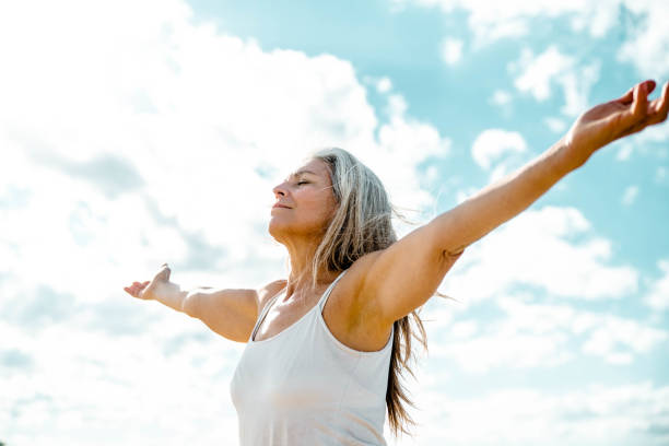 Joyful senior woman enjoying freedom standing with open arms looking up towards the sky