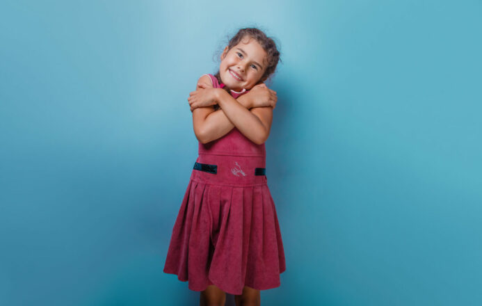 Young girl hugging and loving herself in pink dress on a blue backgound