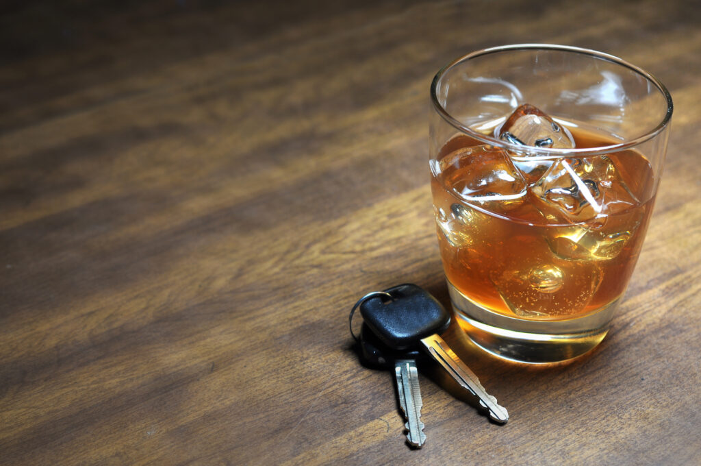 Glass of whiskey and car keys on wooden table.