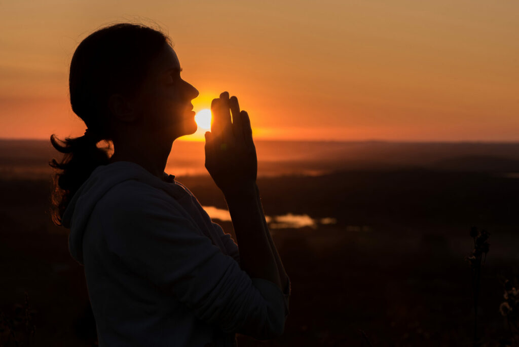 Woman praying at sunset against the sky in summer
