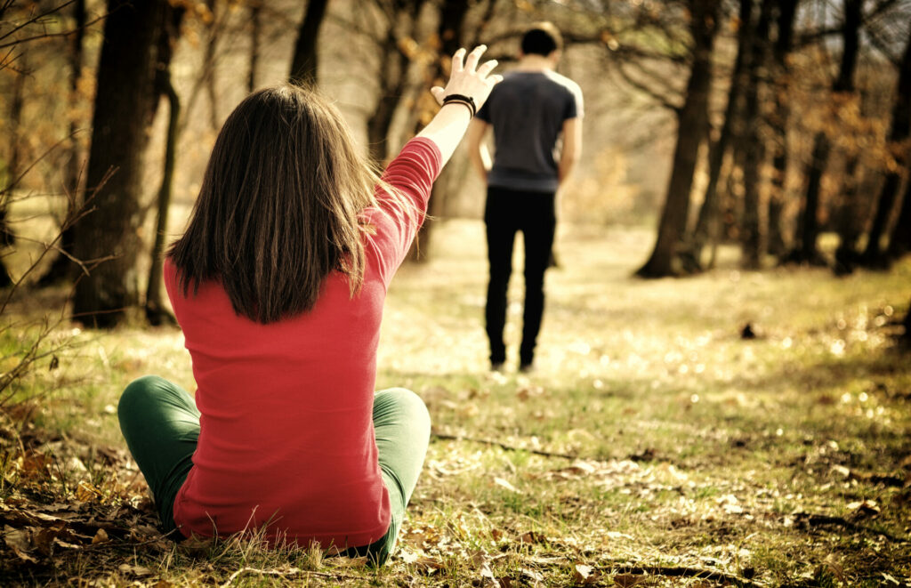 A man walking away in a forest while a woman sits with an arm out toward him