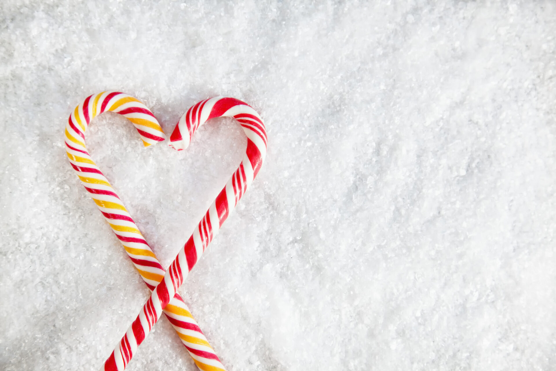Two Candy Canes On Snowy Background Shaped Like a Heart