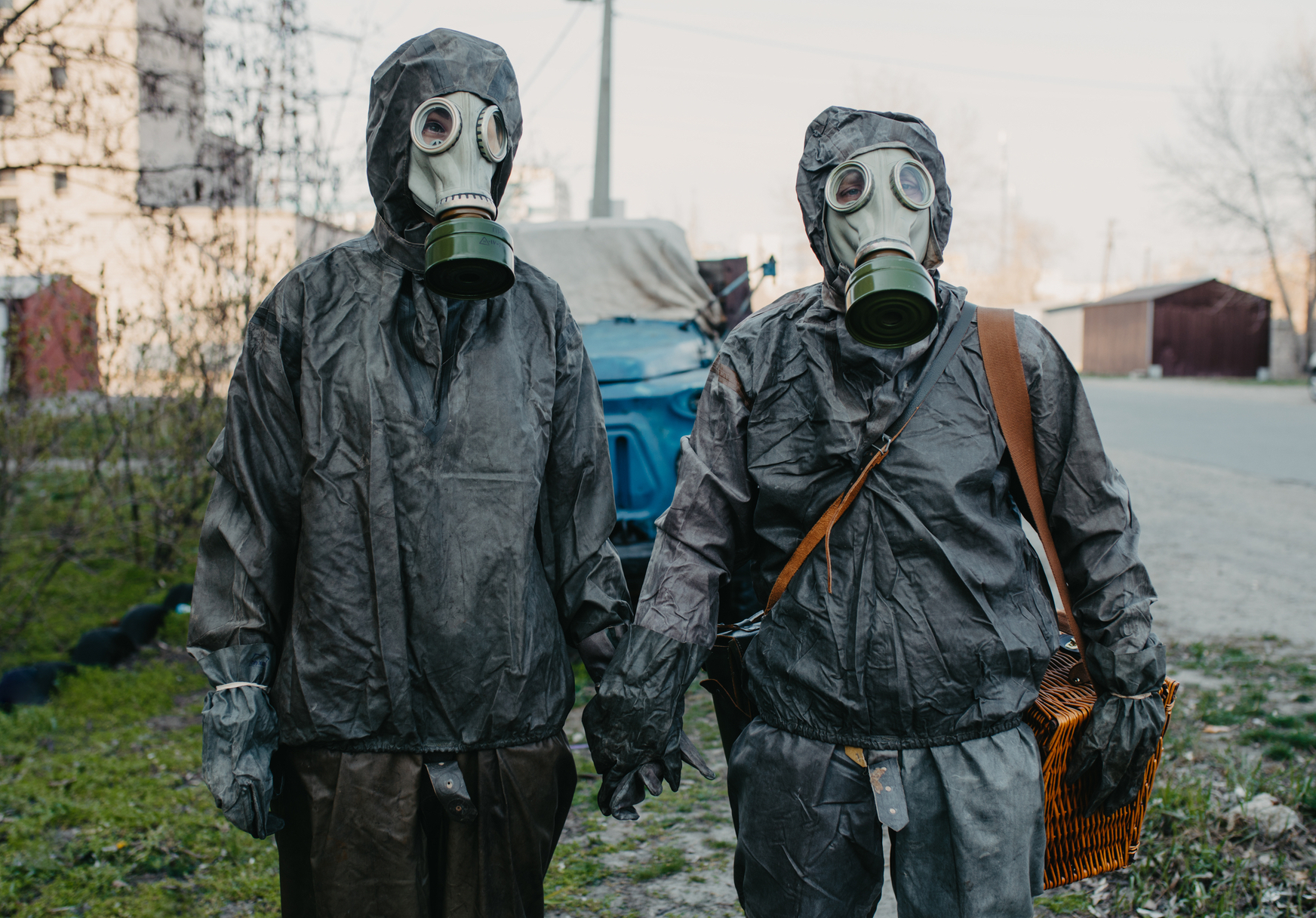 Two people holding hands in protective suits and gas masks